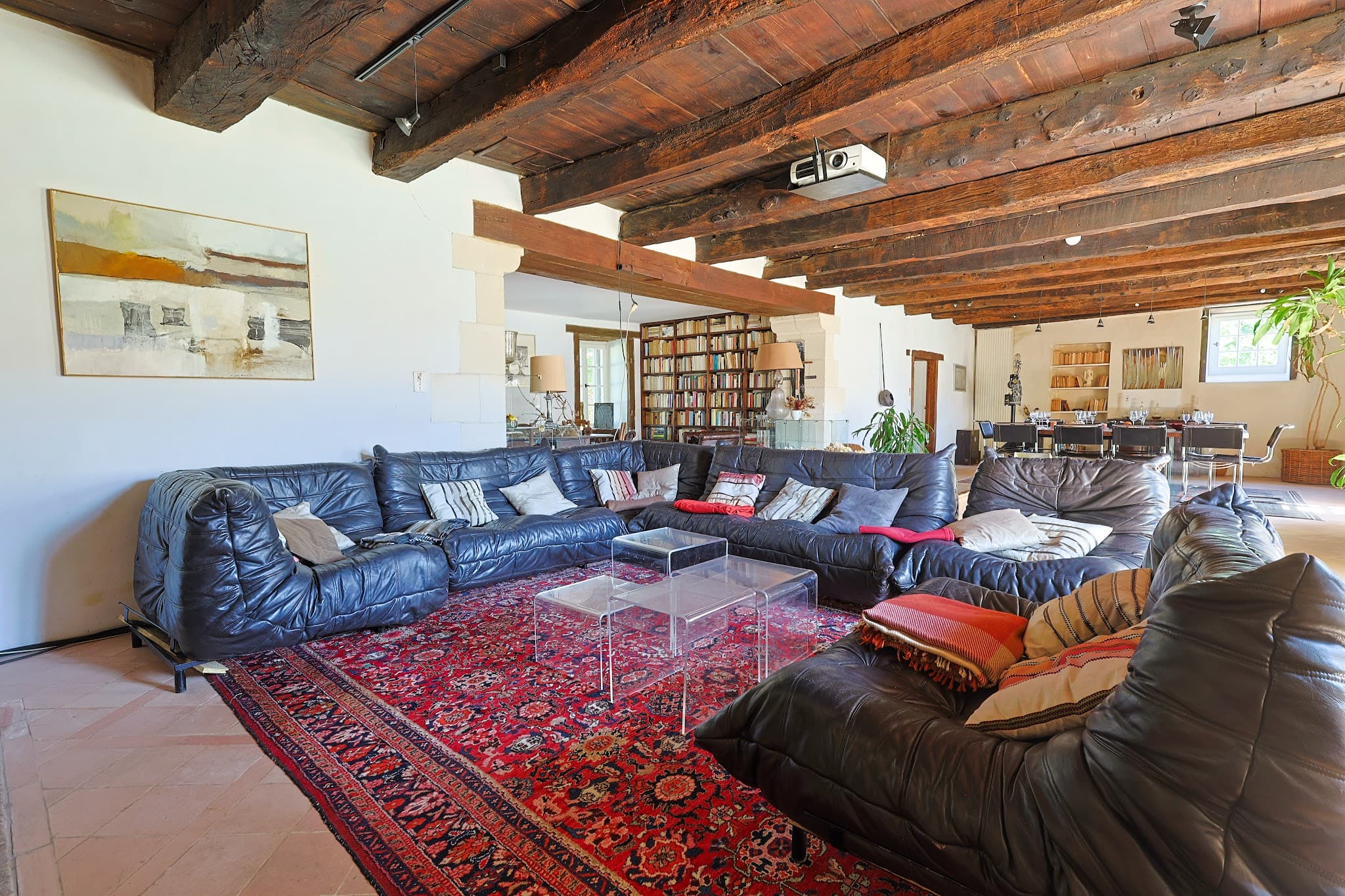 The large living room at Chez Momône, with its sofas, antique rugs and beamed ceiling, opening onto the dining room.