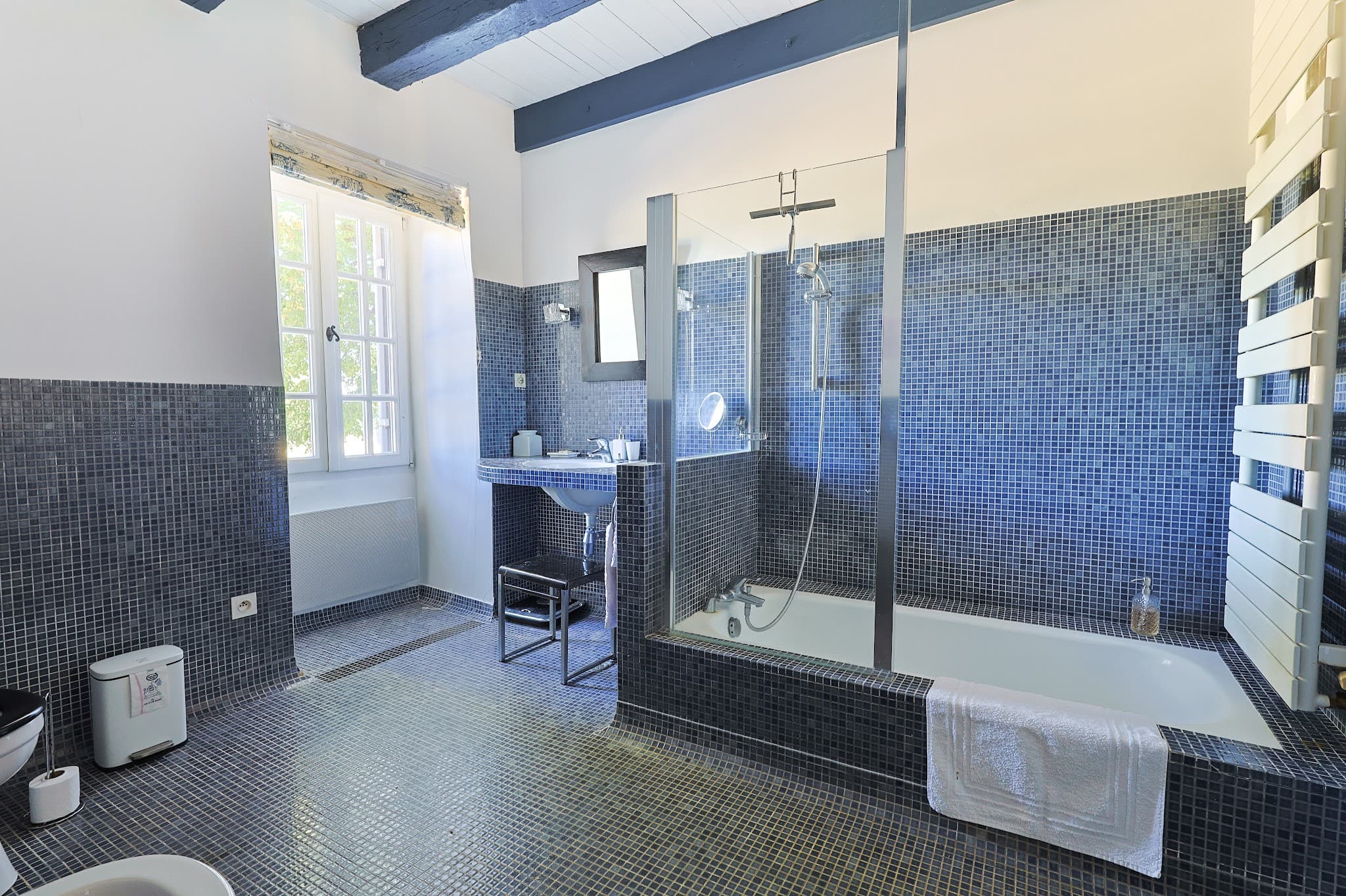 The blue ground-floor bathroom at Chez Momône, in mosaic tiles, with a glass-screened bathtub.